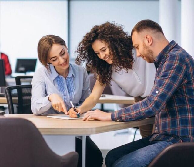 Três pessoas em uma mesa, assinando um documento.